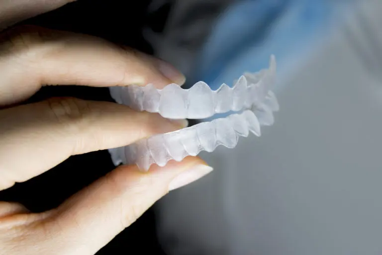 A hand displays clear plastic Invisalign dental aligners, showing both the upper and lower trays, in a photo taken at Andros Orthodontics in Pasco, WA.