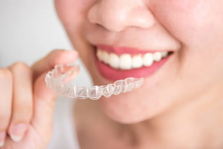 A person at Andros Orthodontics in Pasco, WA smiles while holding Invisalign clear braces near their teeth.