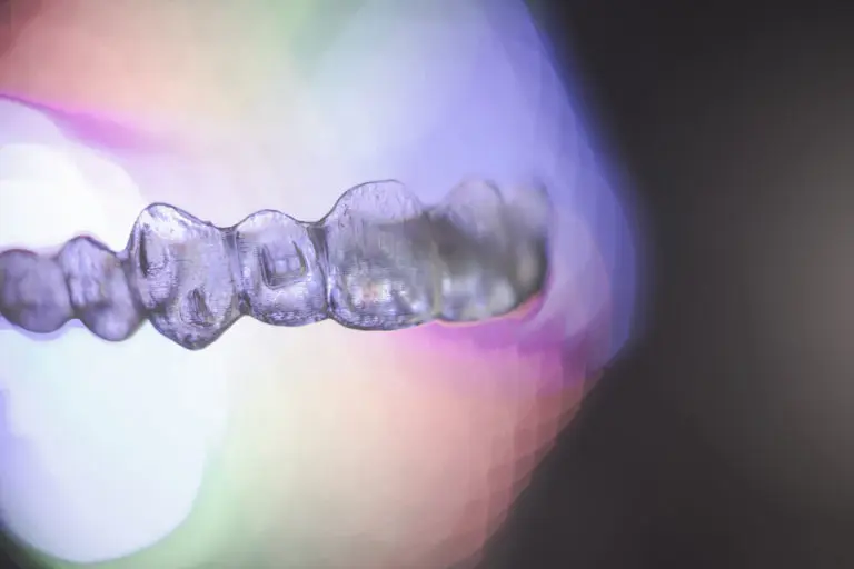 A close-up of a clear Invisalign dental aligner is featured at Andros Orthodontics in Pasco, WA, with vibrant, blurred lights in the background.