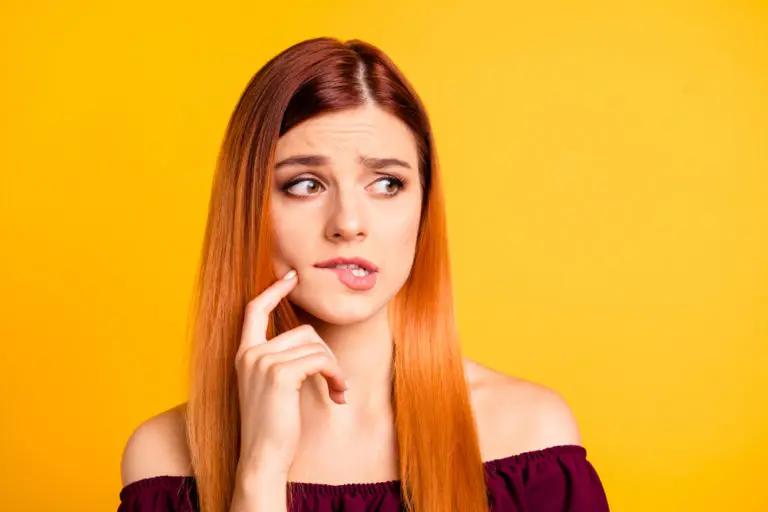 A young woman with long straight hair stands against a solid yellow background, gently touching her cheek while looking to the side—an inviting image representing Andros Orthodontics in Pasco, WA.