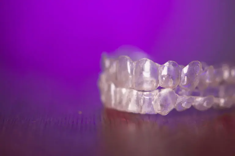 At Andros Orthodontics in Pasco, WA, a clear dental aligner is displayed on a dark surface with a blurred purple background, showcasing modern orthodontic solutions like Invisalign for all ages. Can children receive Invisalign treatment as well?.