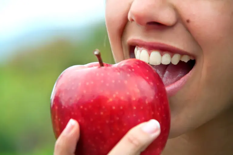 Someone about to bite into a red apple, with a blurred outdoor background, represents healthy smiles supported by Andros Orthodontics in Pasco, WA.
