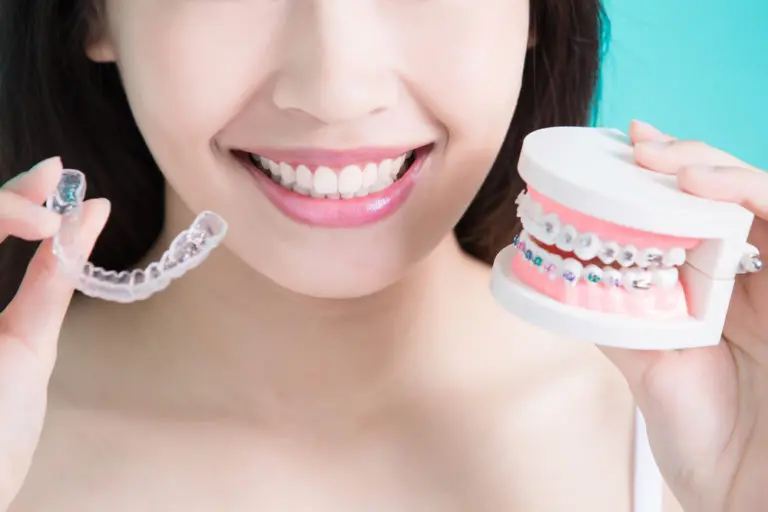 A woman at Andros Orthodontics in Pasco, WA smiles while holding a clear aligner and a dental model featuring both traditional braces and aligners.
