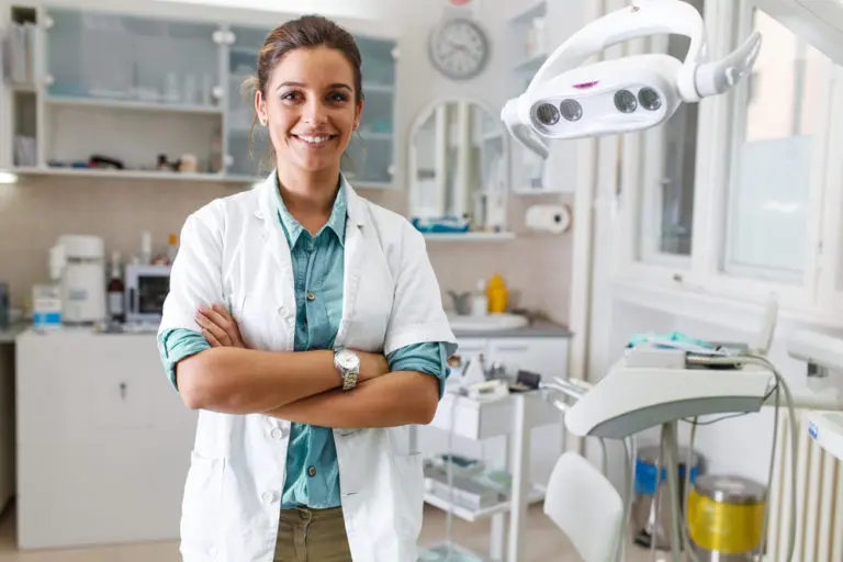 At Andros Orthodontics in Pasco, WA, an orthodontist in a white lab coat stands with arms crossed amid dental equipment and tools.