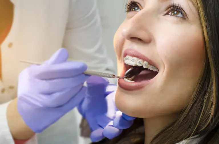 At Andros Orthodontics in Pasco, WA, a dental professional wearing gloves examines a woman’s braces with a dental tool.