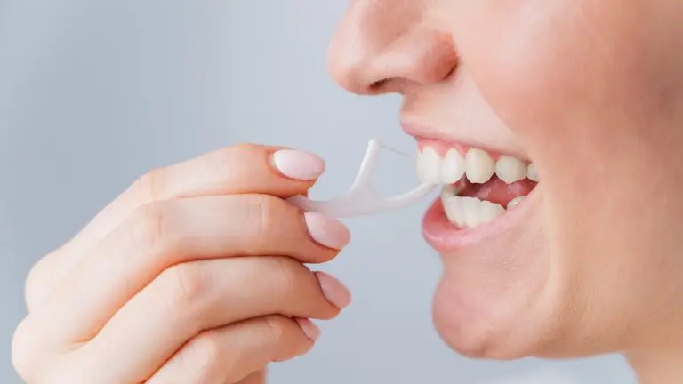 A close-up shows a person's hand and mouth as they use a white dental floss pick to clean between their upper teeth—an example of good oral hygiene recommended by Andros Orthodontics in Pasco, WA.
