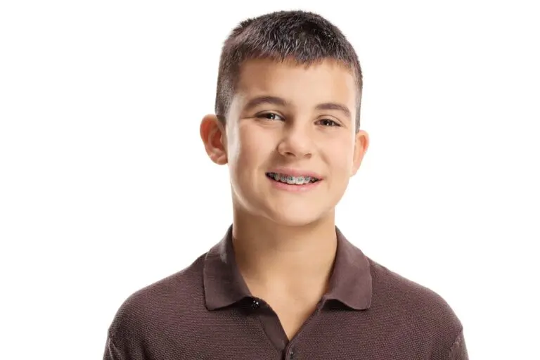 A smiling boy with short dark hair and braces, dressed in a brown collared shirt, represents Andros Orthodontics in Pasco, WA, standing against a plain white background.