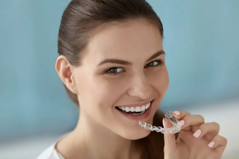 Smiling woman holds a clear aligner by her mouth, highlighting how Andros Orthodontics uses Invisalign for overbite in Pasco, WA -Can Invisalign Fix Overbite in Pasco, WA.
