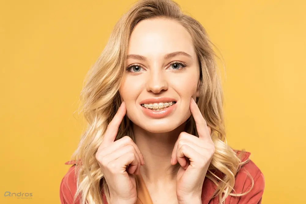 Smiling blonde woman pointing at her teeth against a yellow background - Overbite vs Underbite in Pasco, WA.