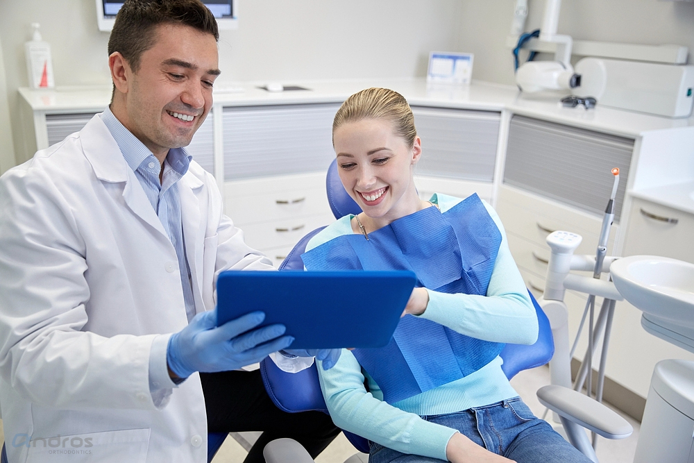 A dentist shows a female patient information on a blue tablet while she sits in a dental chair, both smiling after being explained about how to fix overbite in Pasco, WA..