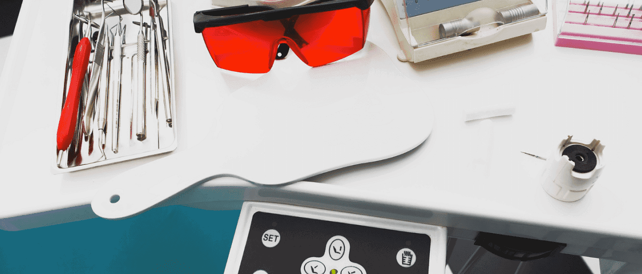 On a white dental tray at Andros Orthodontics in Pasco, WA, you'll find dental instruments, a small mirror, protective red glasses, and tools for fitting metal braces.