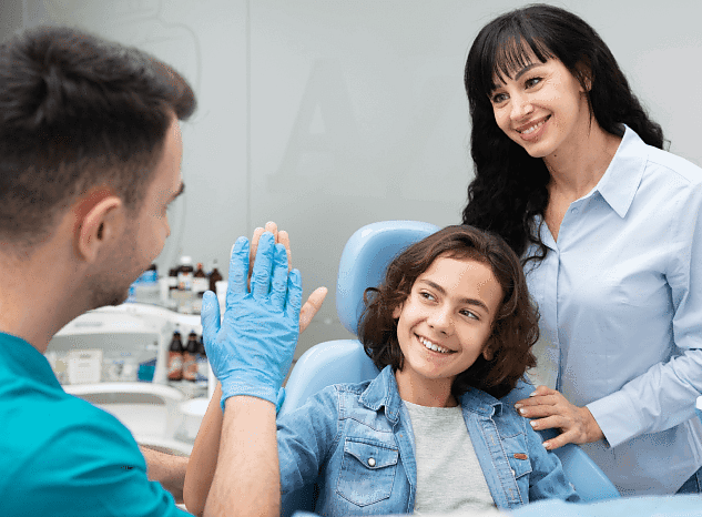 At Andros Orthodontics in Pasco, WA, a dentist gives a high-five to a smiling young patient in the dental chair after discussing jaw surgery, as the child's mother looks on.