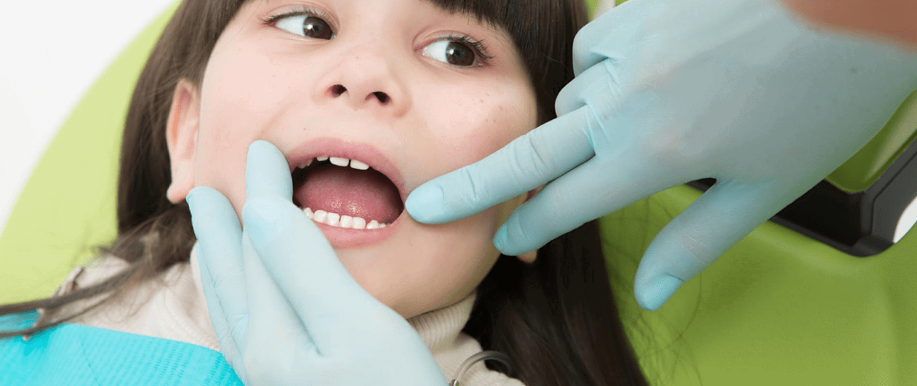 At Andros Orthodontics in Pasco, WA, a children's orthodontist wearing gloves examines a child's open mouth in the dentist chair.
