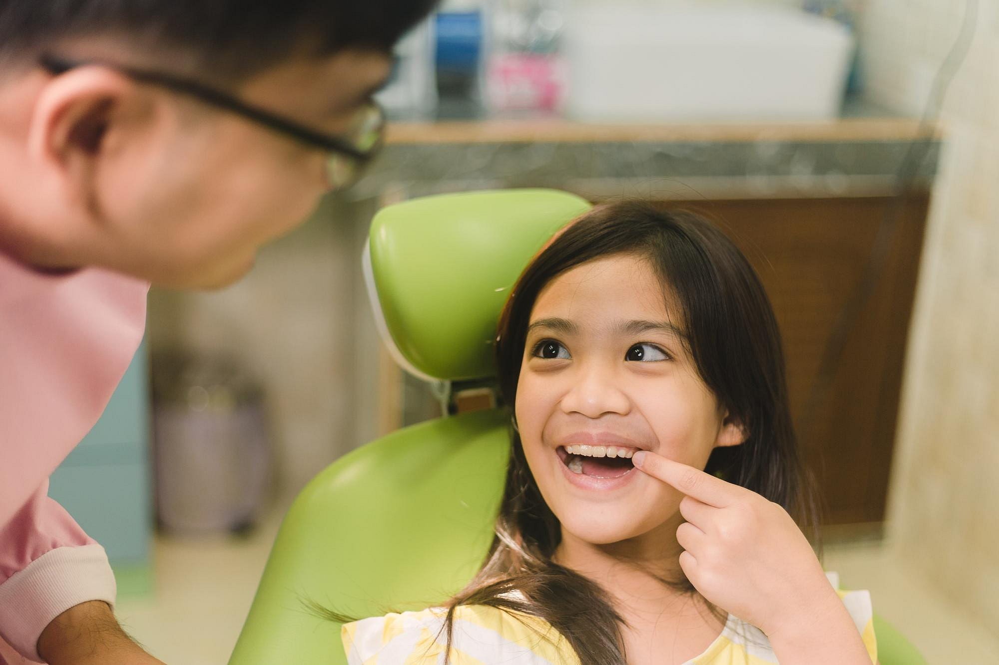A young girl smiles and points to her missing tooth as a children’s orthodontist in glasses talks with her at Andros Orthodontics in Pasco, WA.