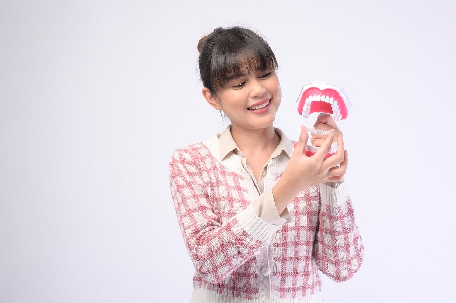 A woman in a pink checkered sweater smiles while examining a dental model, highlighting the benefits of Invisalign at Andros Orthodontics in Pasco, WA.