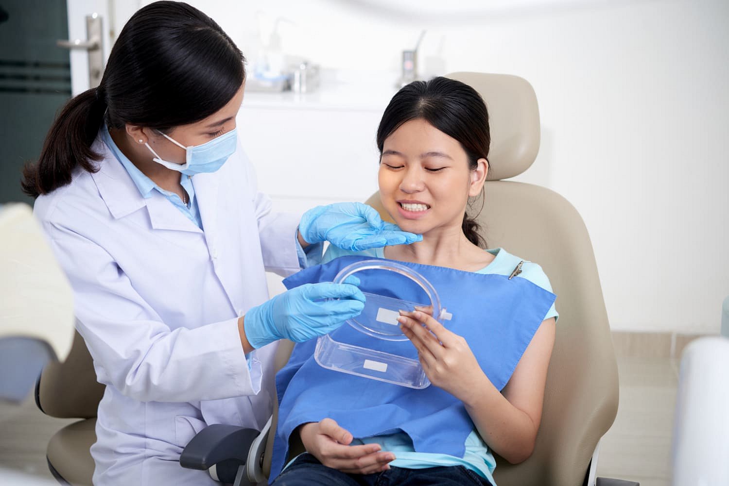 At Andros Orthodontics in Pasco, WA, a dentist wearing gloves and a mask examines the teeth of a female patient, who is a mouth breather and holding a dental impression tray.