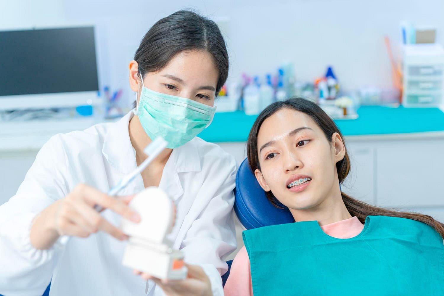 At Andros Orthodontics in Pasco, WA, a dentist demonstrates proper cleaning of orthodontic appliances to a female patient with braces by using a dental model and toothbrush during their consultation.