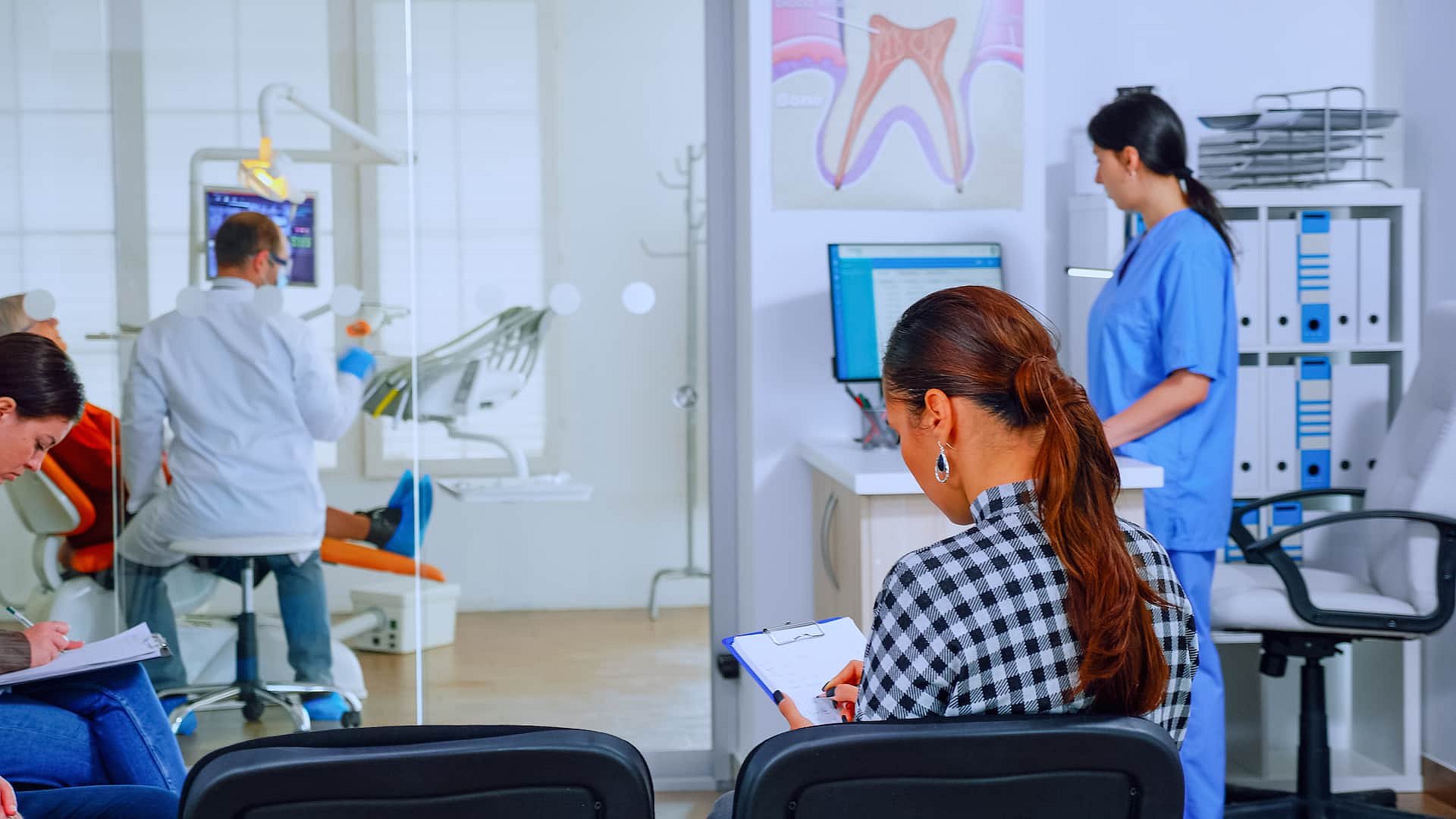 At Andros Orthodontics in Pasco, WA, patients wait in the clinic’s lobby—one fills out a clipboard as a dental professional discusses orthodontic insurance plans at a computer and another assists a patient in an exam room.