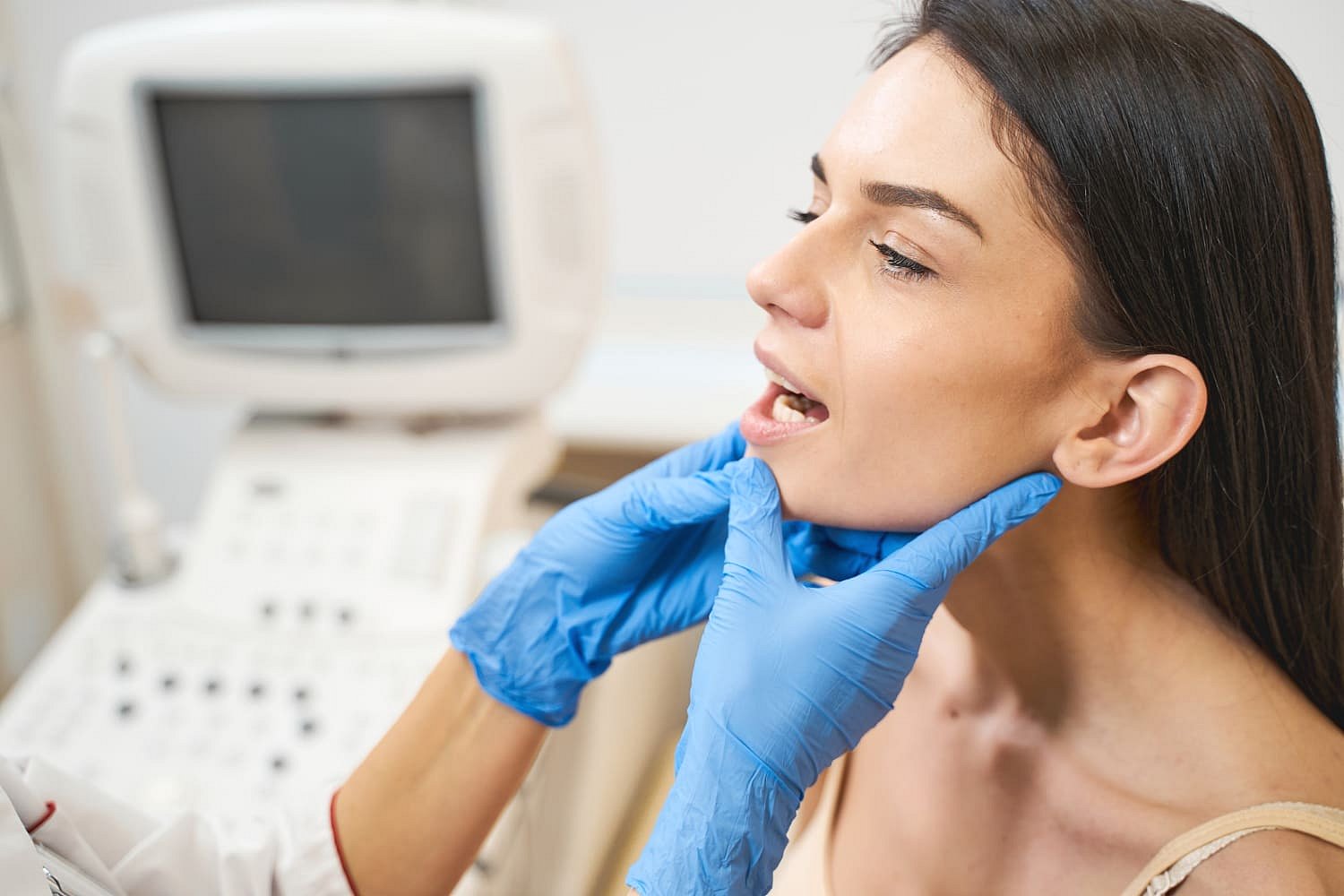 At Andros Orthodontics in Pasco, WA, a healthcare professional wearing blue gloves examines a woman's jaw and mouth for potential jaw surgery in a medical setting.
