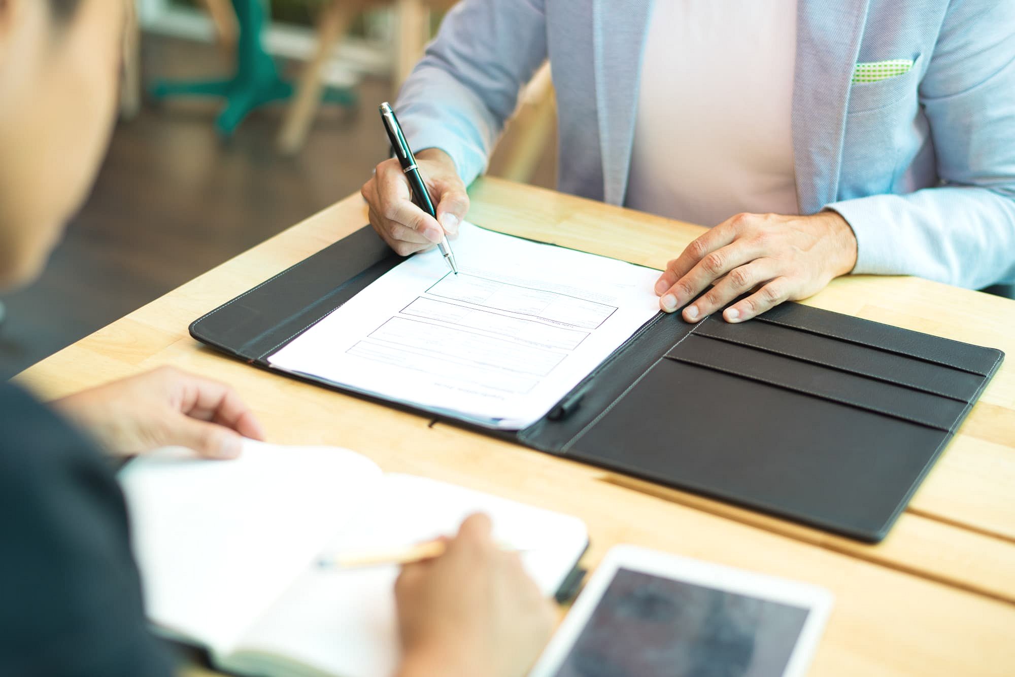 At Andros Orthodontics in Pasco, WA, two people sit at a table discussing whether Invisalign is covered by insurance—one writes on a document inside a folder while the other takes notes in a notebook, and an electronic tablet rests on the table.