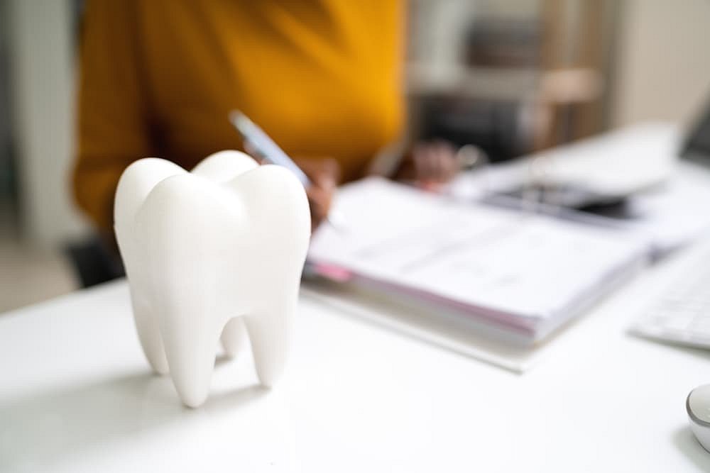On a desk at Andros Orthodontics in Pasco, WA, a tooth model and Herbst Appliance are displayed in the foreground as someone completes paperwork in the blurred background.