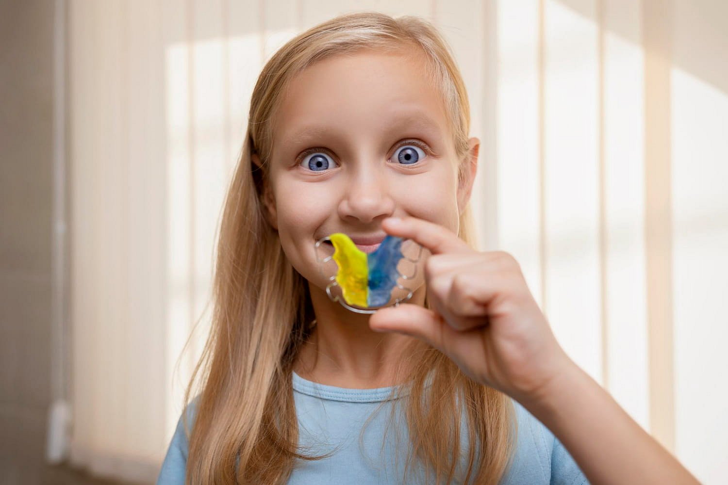 A young girl proudly smiles while holding a colorful dental retainer, showing that wearing retainers can be fun—especially with the care of Andros Orthodontics, a dedicated Children’s Orthodontist in Pasco, WA.