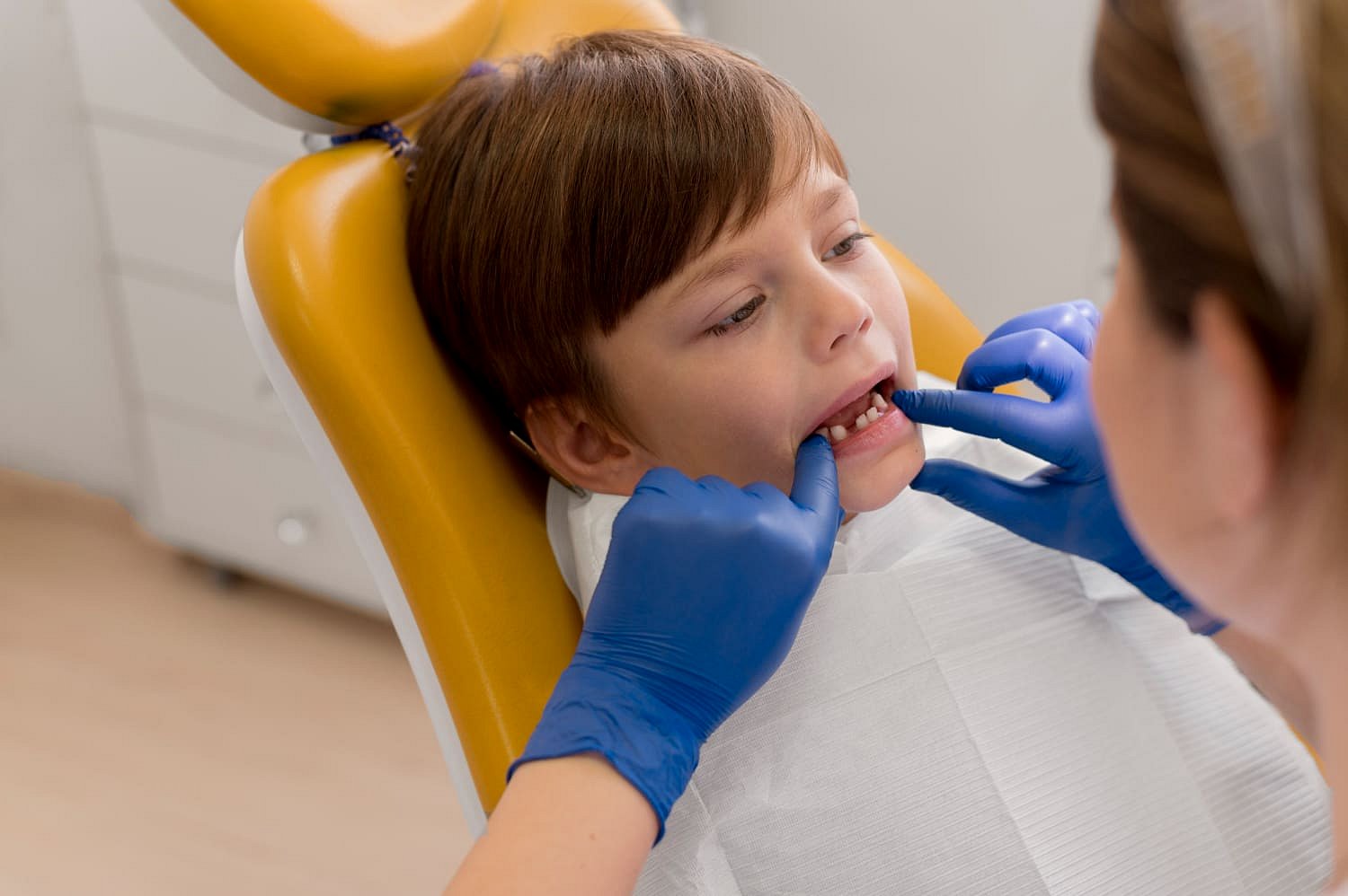 At Andros Orthodontics in Pasco, WA, a children’s orthodontist wearing blue gloves examines a child’s teeth as the child sits in the dental chair.