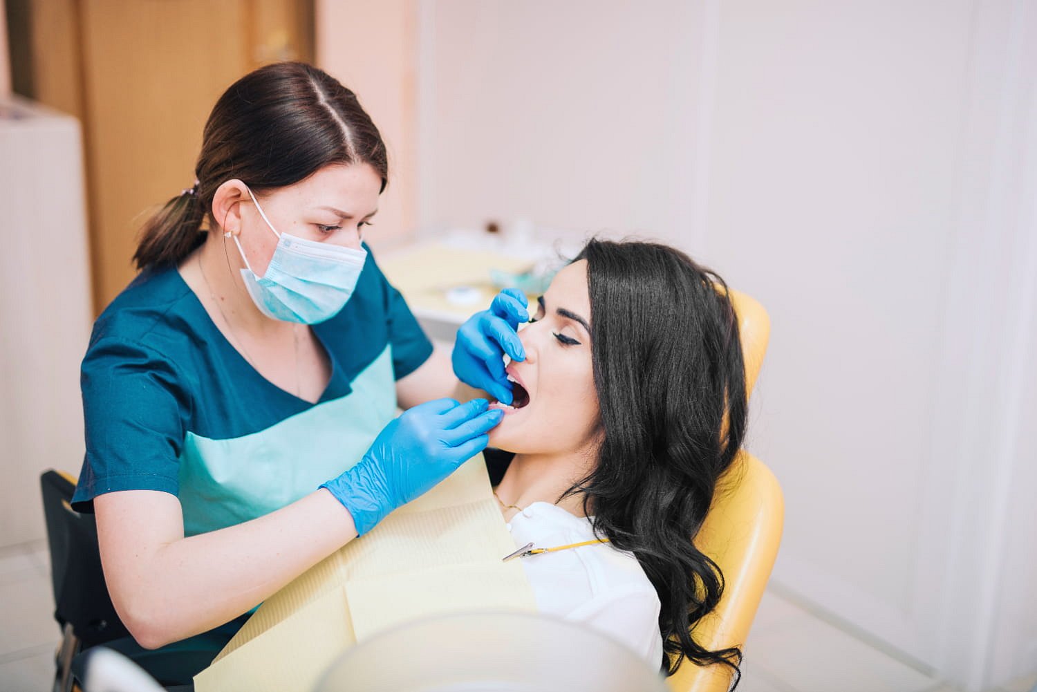 At Andros Orthodontics in Pasco, WA, a dental professional wearing gloves and a mask examines a female patient’s teeth in the dental chair to check for issues like tongue thrust.