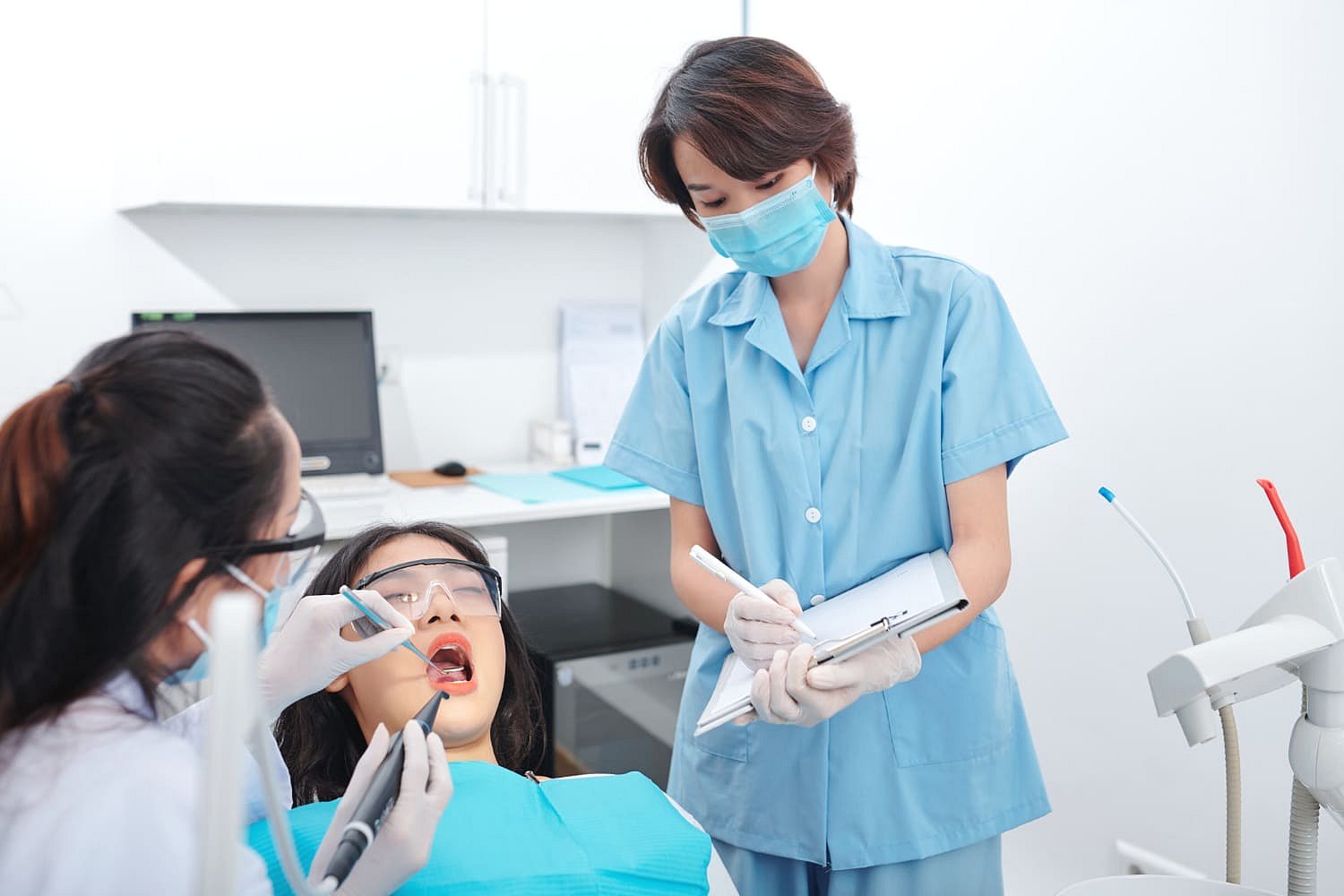 At Andros Orthodontics in Pasco, WA, a dentist inspects a patient's metal braces as a masked dental assistant takes notes in the clinic.