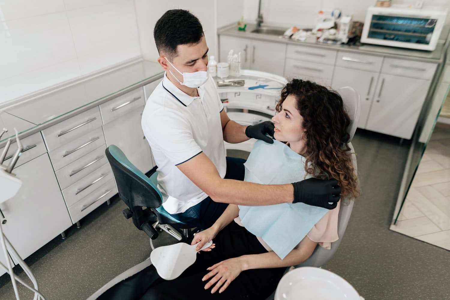 At Andros Orthodontics in Pasco, WA, a dentist in gloves and a mask prepares to examine a seated female patient for concerns like tongue thrust.