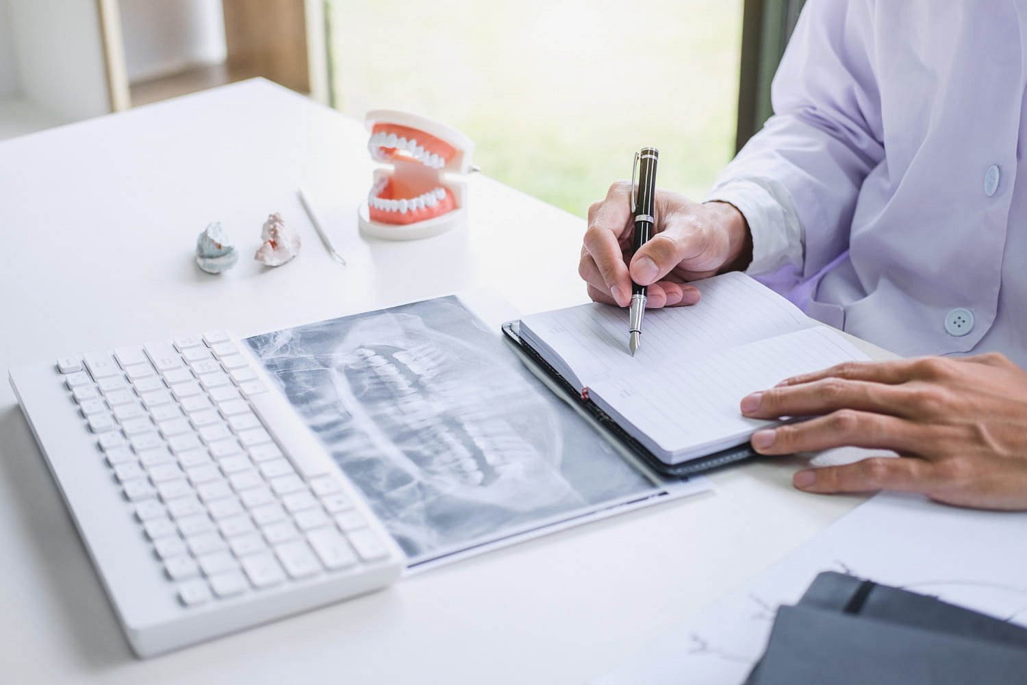At Andros Orthodontics in Pasco, WA, a dentist reviews orthodontic insurance plans at a desk with dental X-rays, molds, a teeth model, and a keyboard.