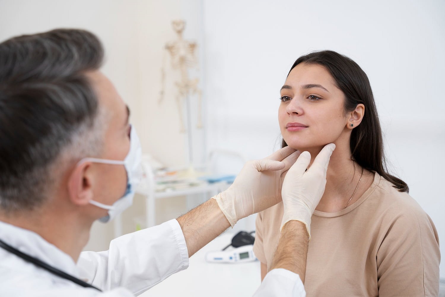 At Andros Orthodontics in Pasco, WA, a doctor wearing gloves examines a young woman's neck in a medical office, possibly evaluating her for jaw surgery.