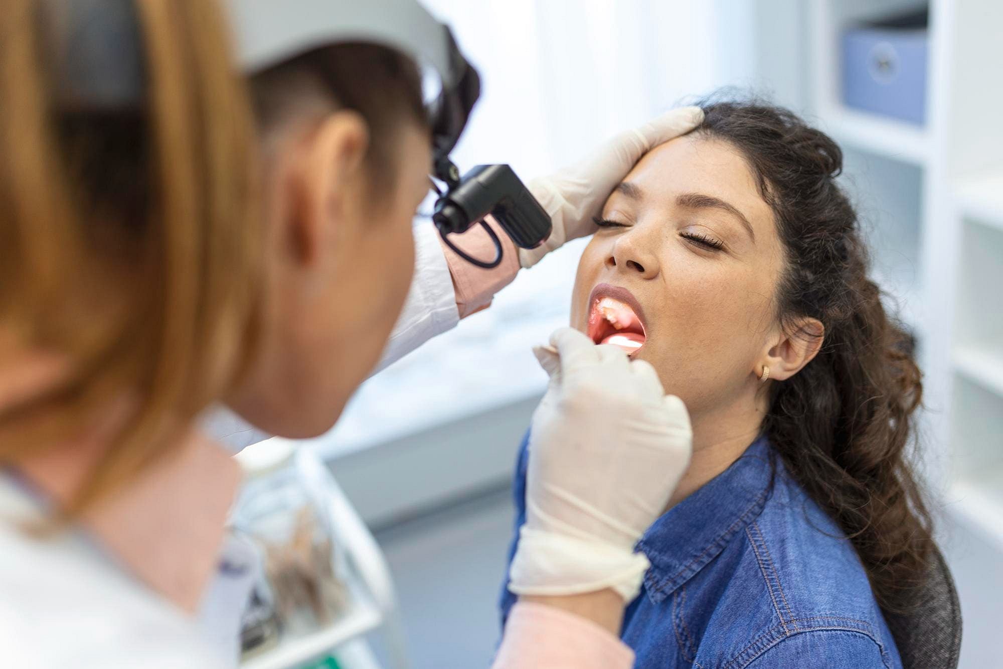 At Andros Orthodontics in Pasco, WA, a healthcare professional uses a tongue depressor to examine a seated woman's open mouth for signs of tongue thrust.