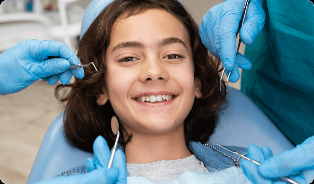 At Andros Orthodontics in Pasco, WA, a children’s orthodontist guides gloved hands holding dental instruments near the mouth of a smiling child seated in a dental chair.
