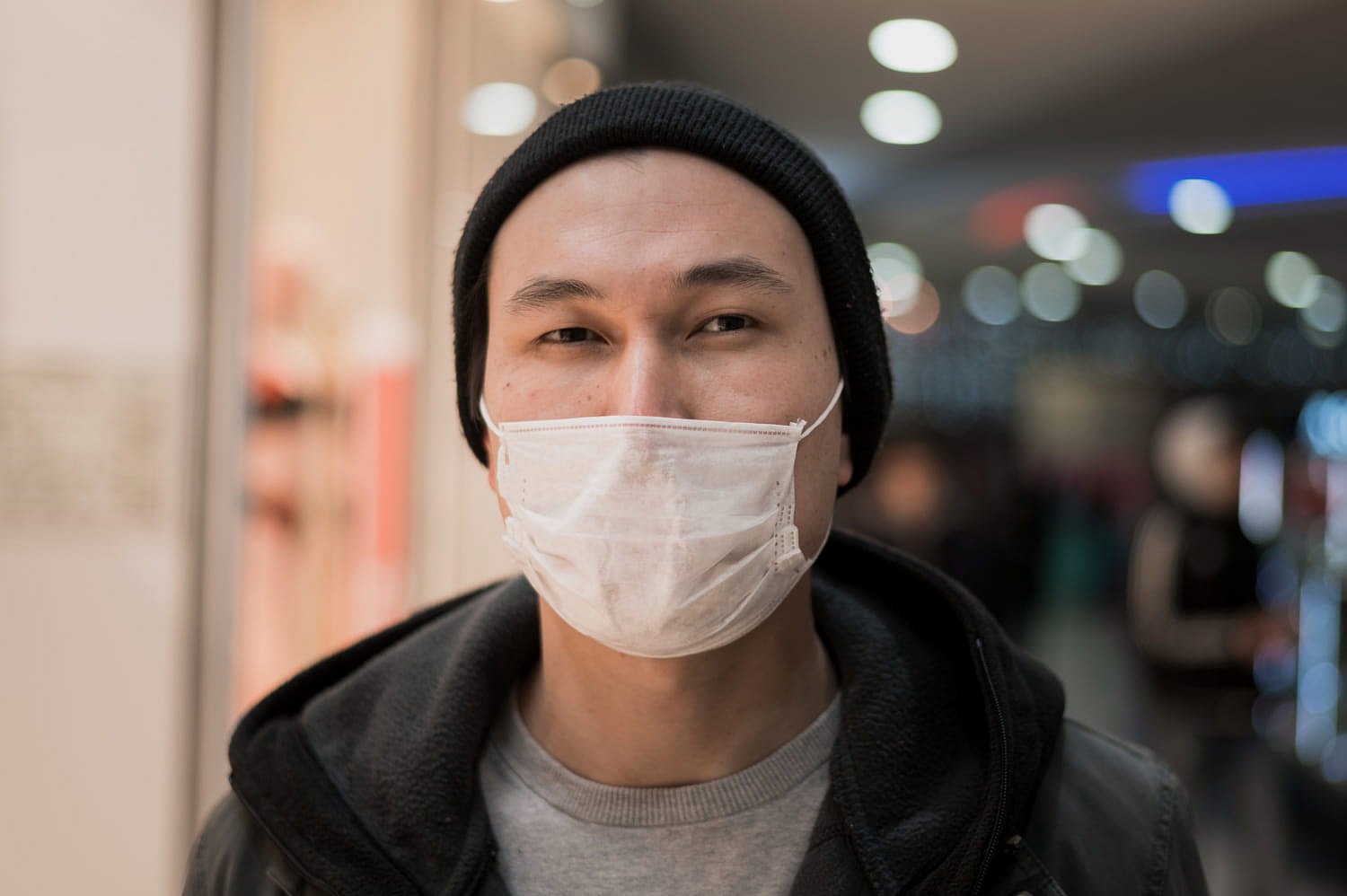 At Andros Orthodontics in Pasco, WA, a person in a black beanie, gray hoodie, and white face mask stands indoors against a blurred backdrop of lights and people—capturing the typical appearance of a masked mouth breather.