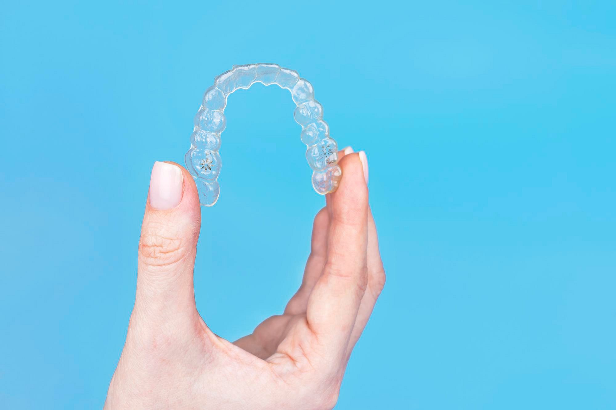 A hand displays a clear orthodontic aligner against a solid blue background, showcasing Andros Orthodontics' discreet Invisalign options and affordable Invisalign cost in Pasco, WA.