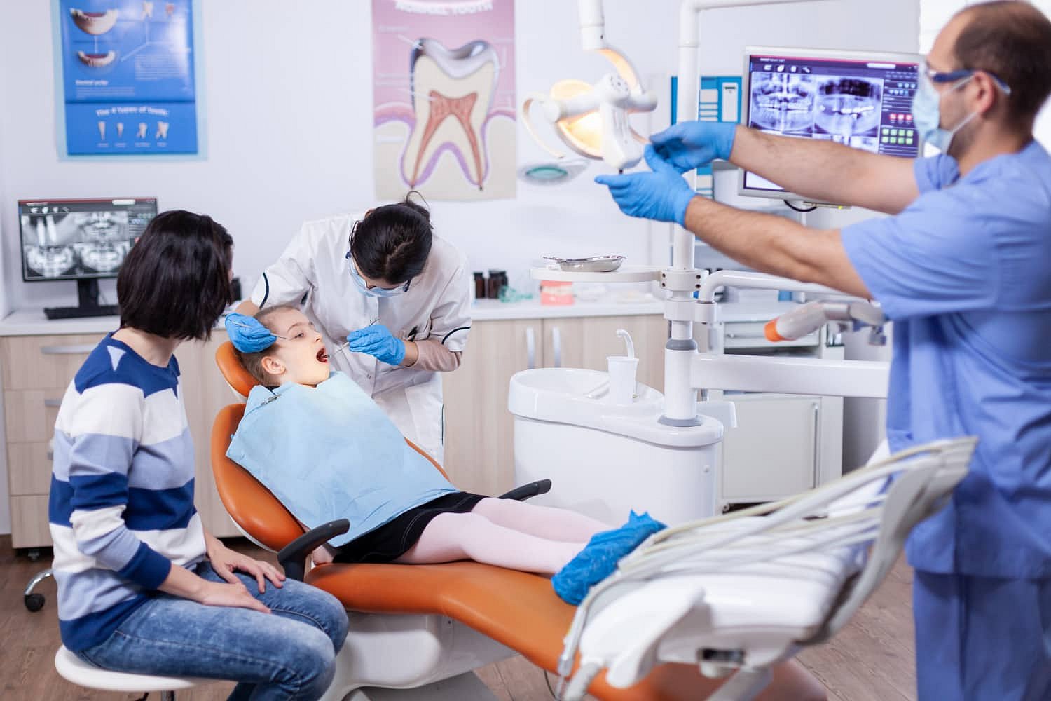 At Andros Orthodontics in Pasco, WA, a dentist and assistant examine a child in the dental chair—possibly discussing treatment options like a Herbst Appliance—while an adult watches nearby amid visible dental equipment and monitors.