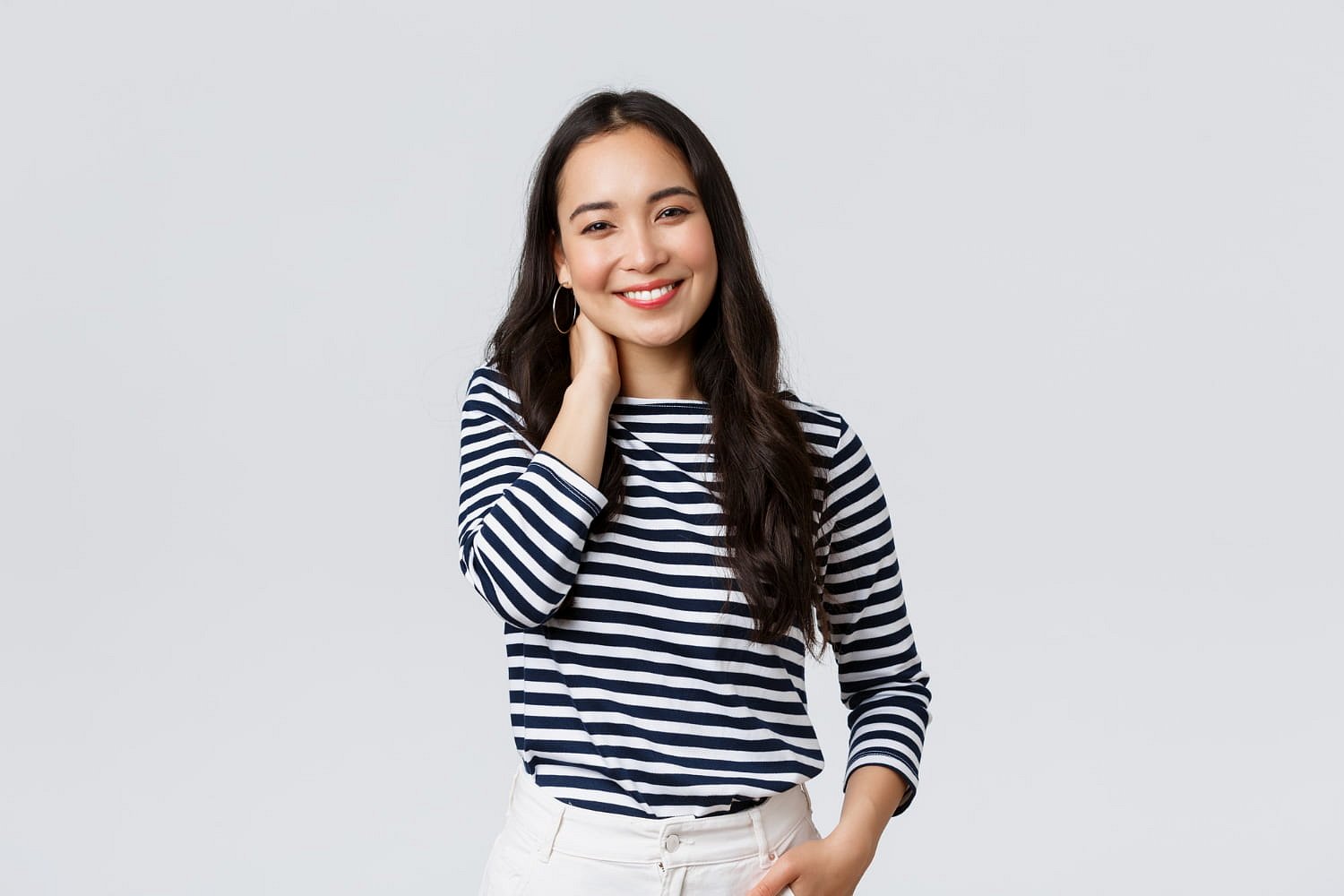A woman with long dark hair, wearing metal braces, a black and white striped shirt, and white pants, smiles against a plain light background at Andros Orthodontics in Pasco, WA.