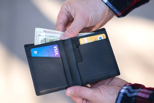 While considering options such as an Invisalign payment plan, a person with an open black wallet—cash and cards on display, including a blue Visa—thinks about Andros Orthodontics in Pasco, WA.
