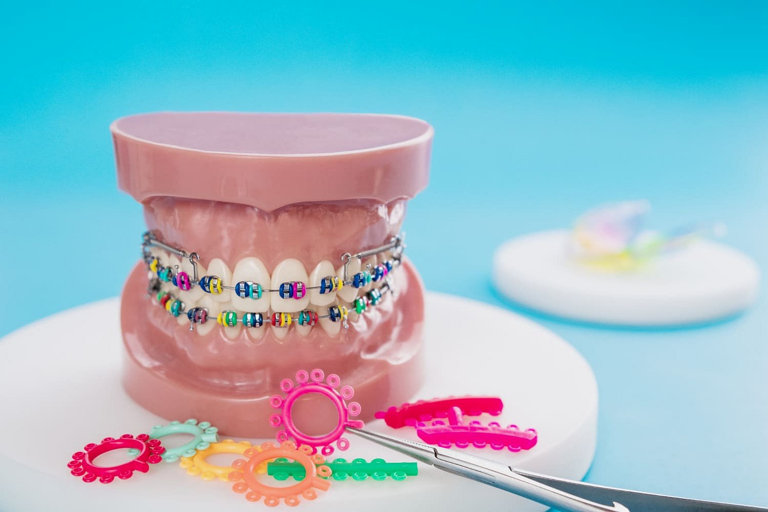 A dental model with metal braces and colorful elastic bands is displayed on a white surface, surrounded by assorted orthodontic elastics and dental tools at Andros Orthodontics in Pasco, WA.