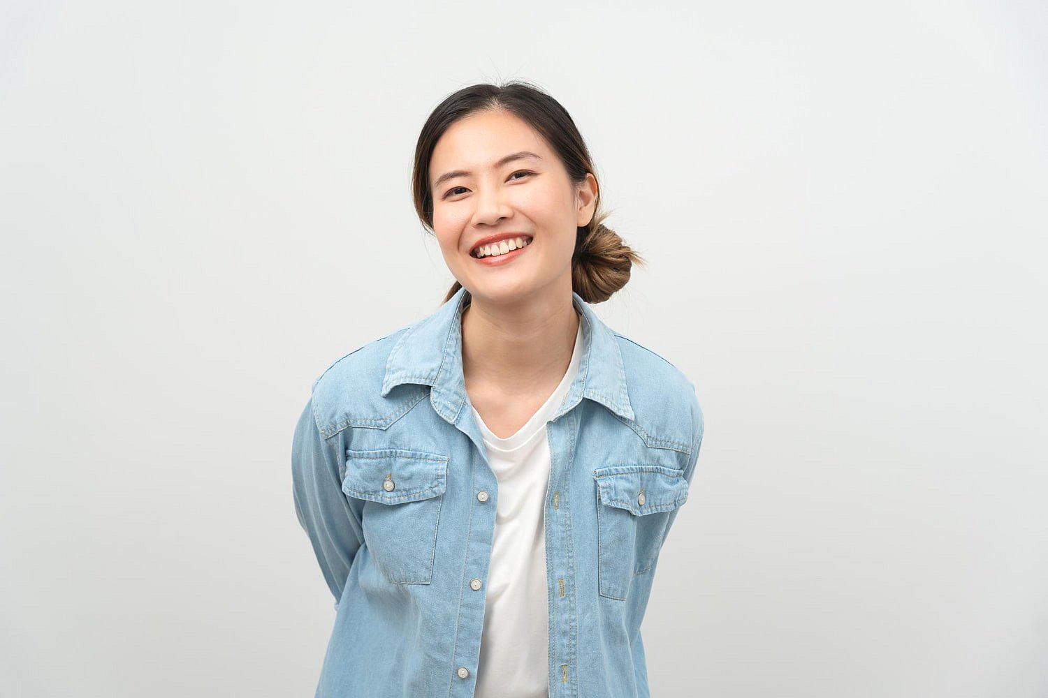 A young woman with dark hair tied back, dressed in a light denim shirt over a white top, confidently displays her Invisalign in this image for Andros Orthodontics in Pasco, WA.