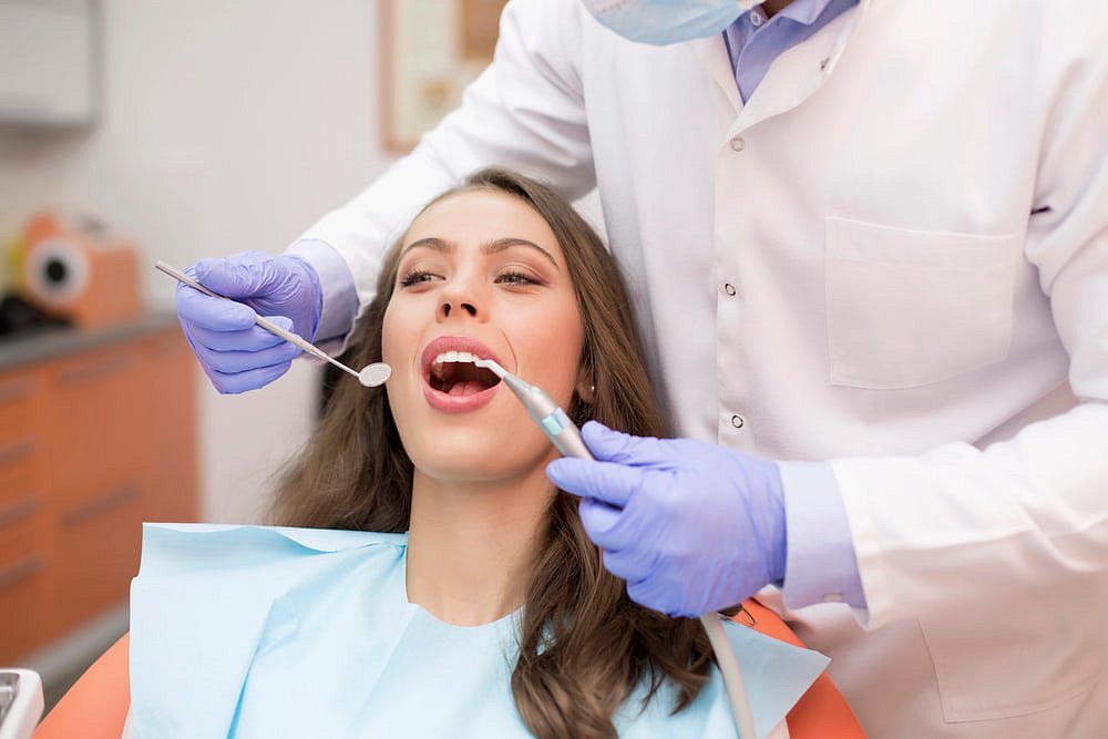 At Andros Orthodontics in Pasco, WA, a dentist wearing gloves examines a woman's teeth with dental tools, possibly assessing whether she needs a palatal expander as she sits in the dental chair.