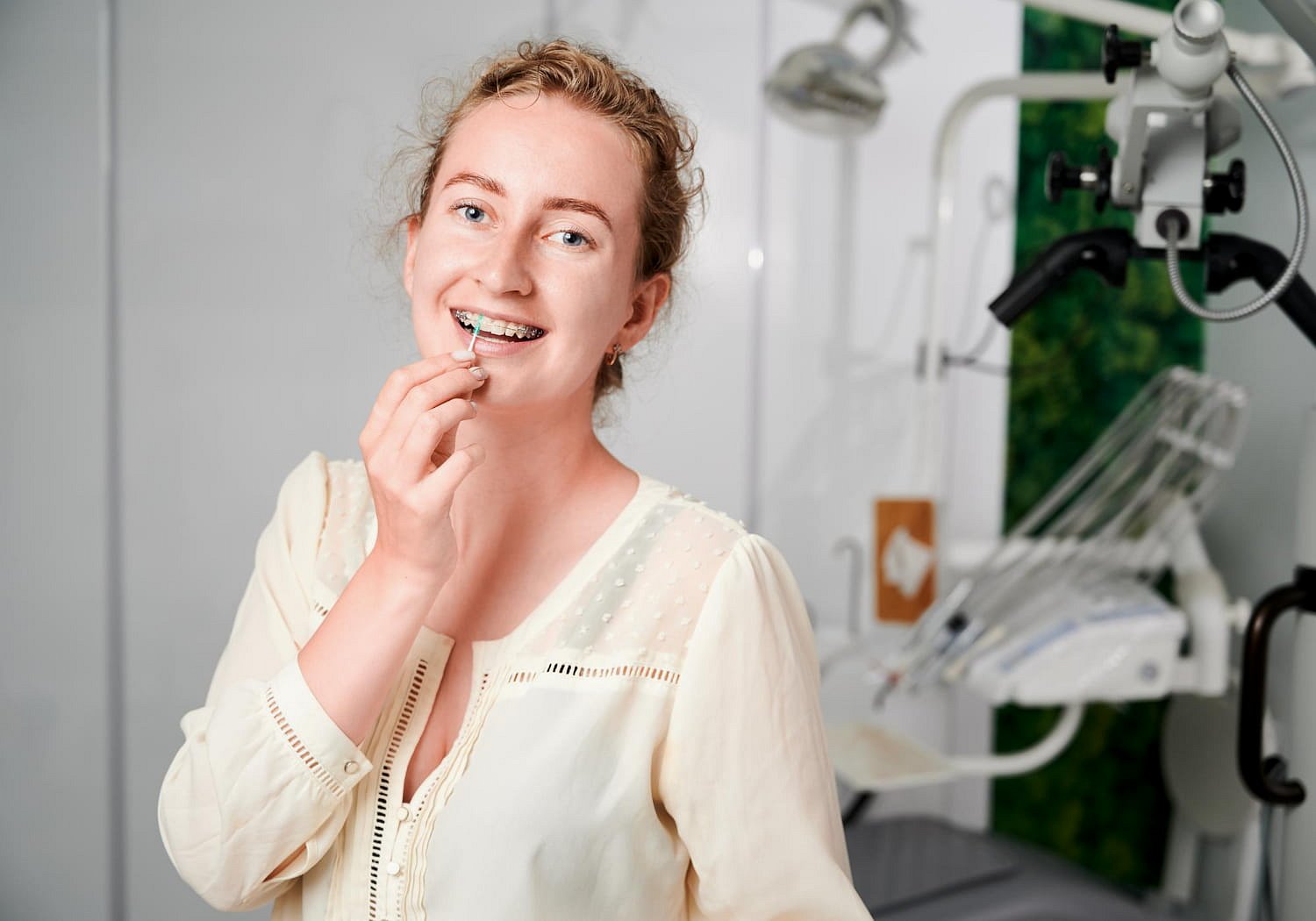 A young woman at Andros Orthodontics in Pasco, WA smiles while holding a clear dental aligner near her mouth, exploring options like clear ceramic braces for a confident, beautiful smile.