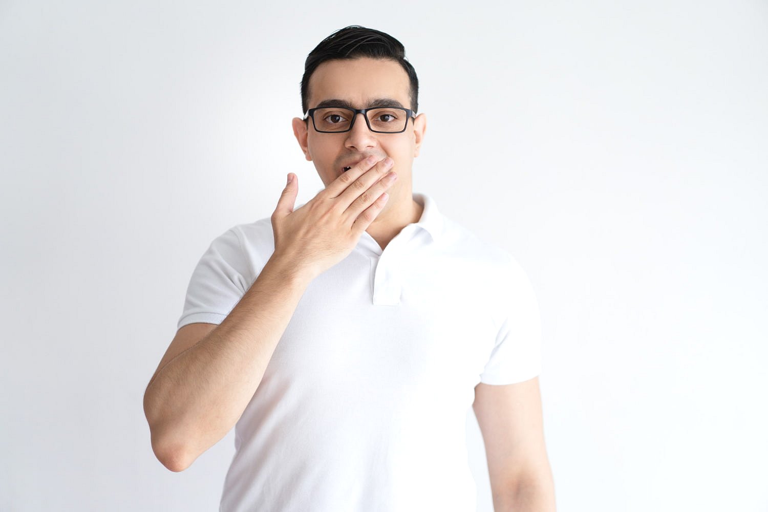 A man in glasses and a white polo shirt, possibly concealing an underbite by covering his mouth with one hand, stands against a plain white background at Andros Orthodontics in Pasco, WA.