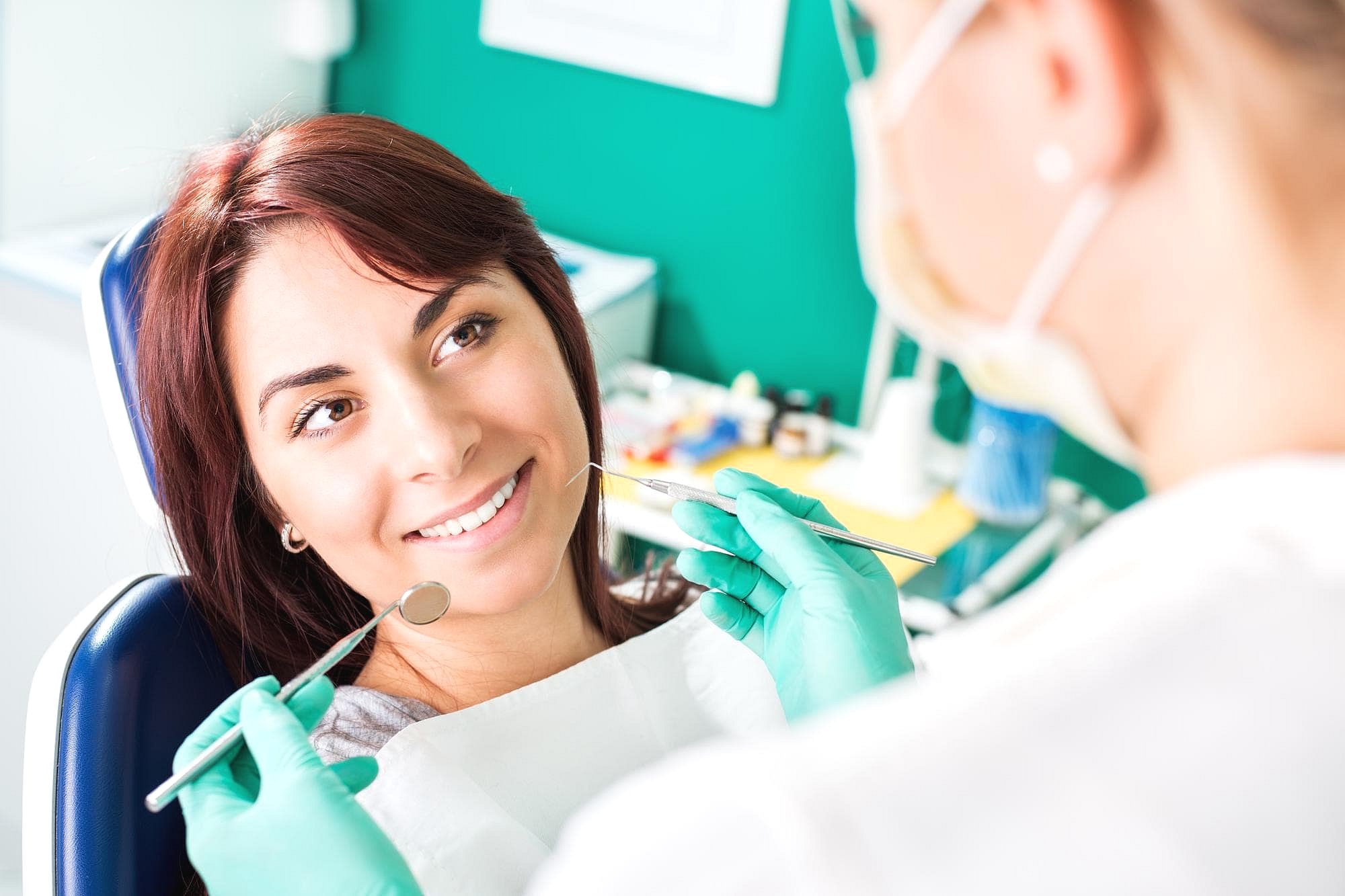 At Andros Orthodontics in Pasco, WA, a dentist in gloves uses a mirror and probe to examine a smiling patient, emphasizing the importance of adult orthodontics for a healthy, confident smile.