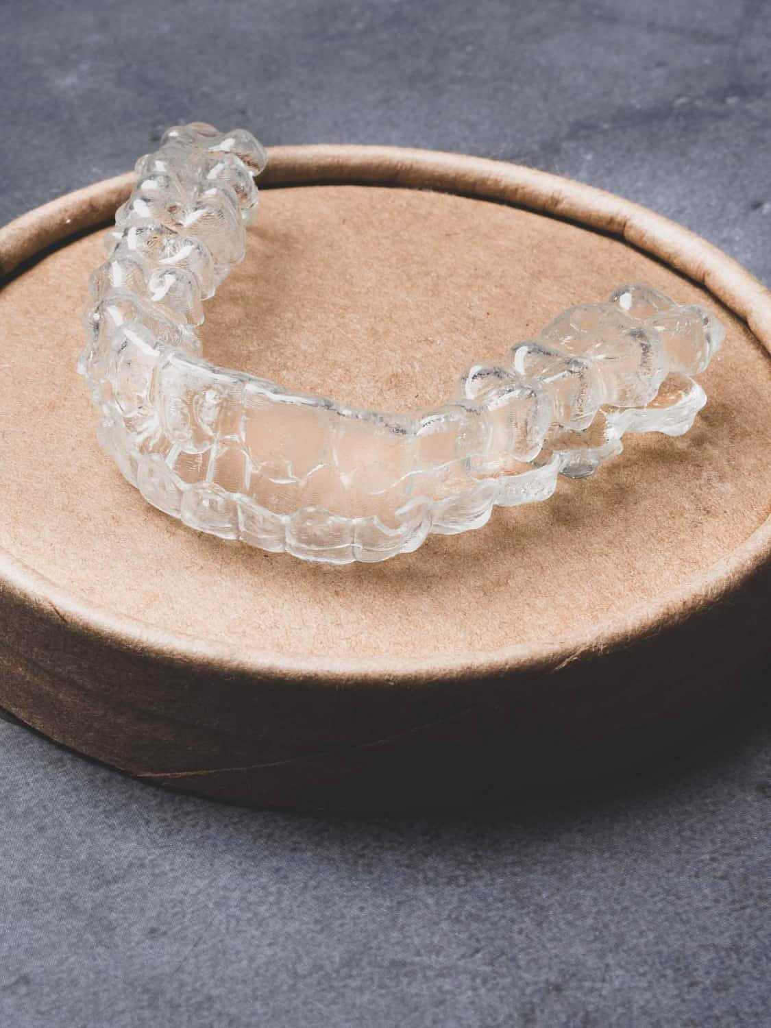 A clear dental aligner sits on a round cardboard container against a gray background, showcasing the discreet Invisalign Payment Plan option at Andros Orthodontics in Pasco, WA.
