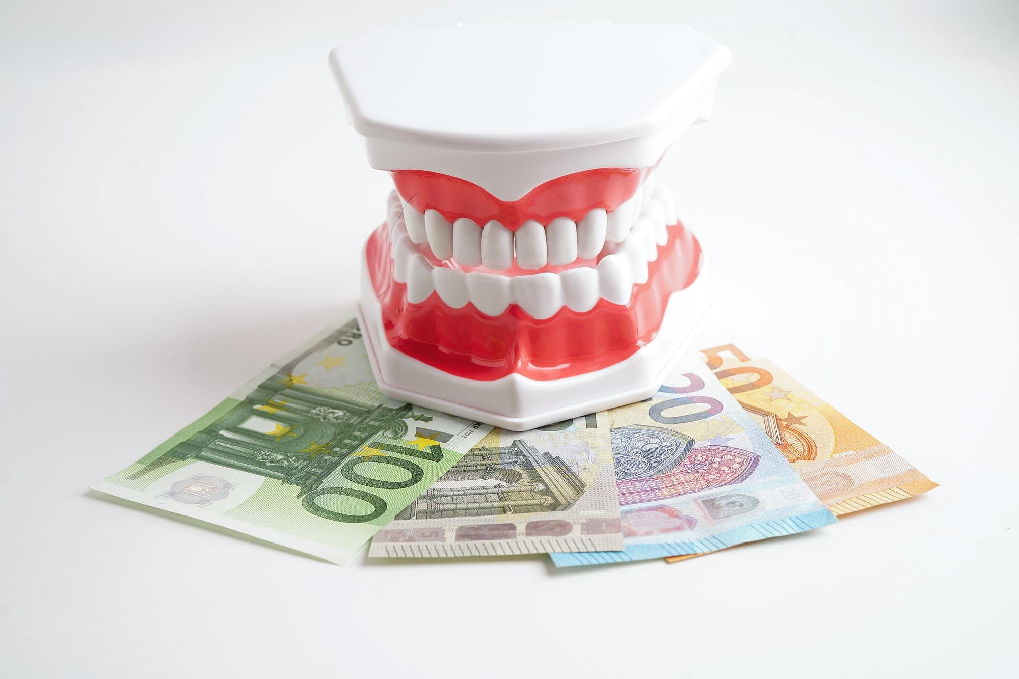 A model of human teeth sits atop several Euro banknotes on a white background, representing the costs covered by orthodontic insurance plans at Andros Orthodontics in Pasco, WA.