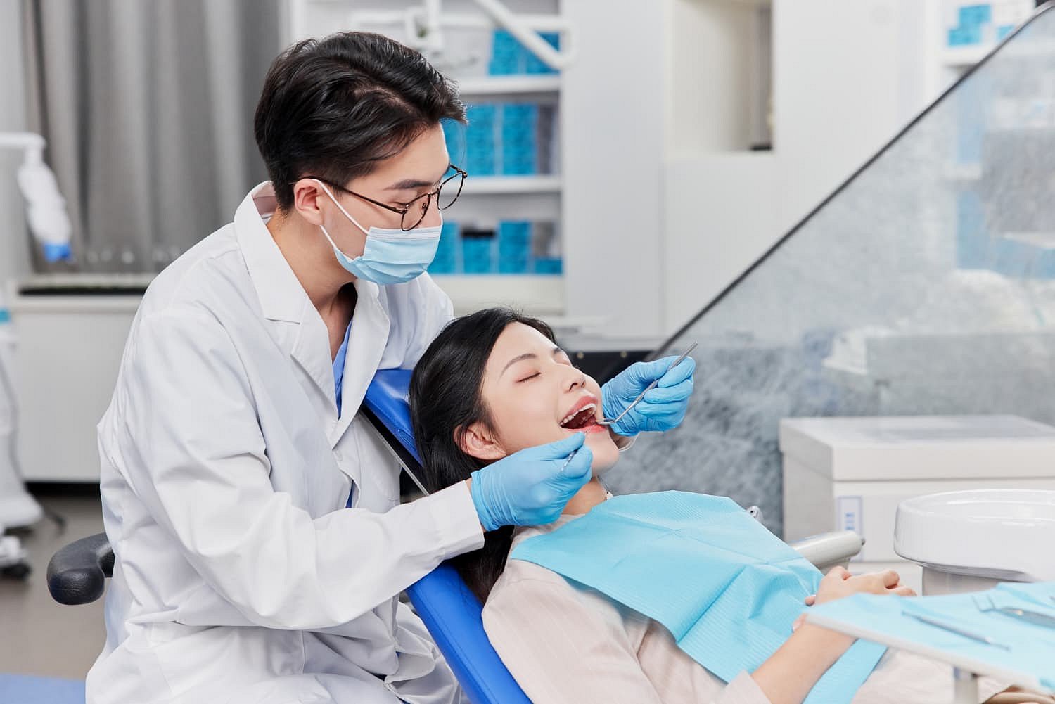 At Andros Orthodontics in Pasco, WA, a dentist wearing a mask and gloves examines a patient's teeth for issues like tongue thrust while the patient reclines in the dental chair with a bib.