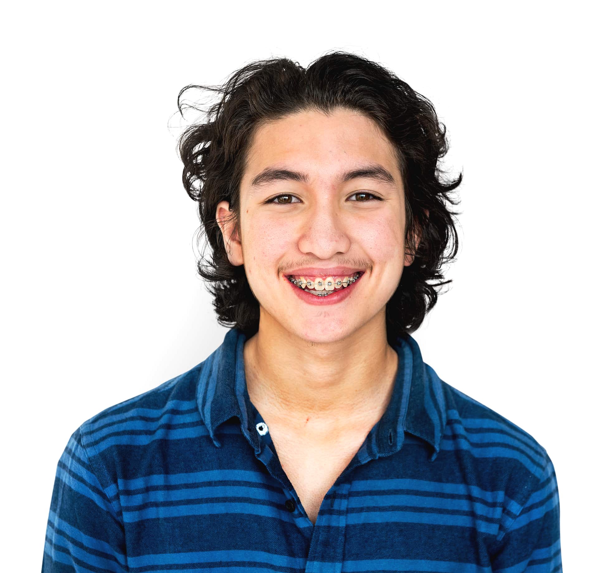 A young adult with medium-length dark hair, wearing a blue striped shirt and adult braces, smiles at the camera in this photo for Andros Orthodontics in Pasco, WA.