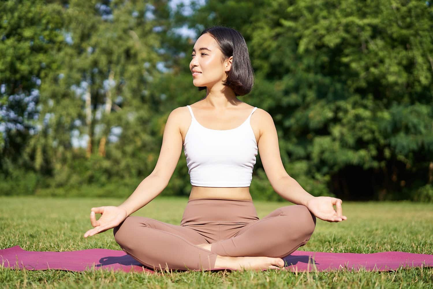 Enjoying a peaceful moment surrounded by green grass and trees, a woman practices mindful mouth breathing while meditating on a yoga mat. Andros Orthodontics in Pasco, WA supports healthy habits like these for overall well-being.